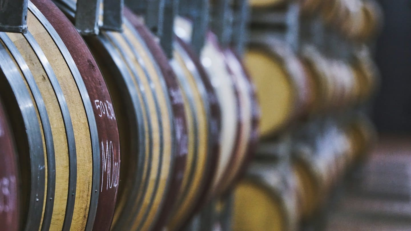 Botti di vino in legno accatastate in una cantina poco illuminata.