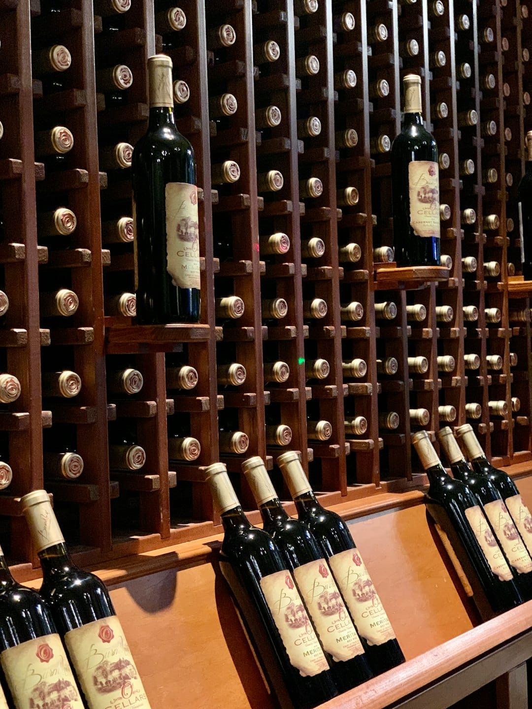 Bottiglie di vino rosso disposte su rastrelliere scure in legno in una cantina.