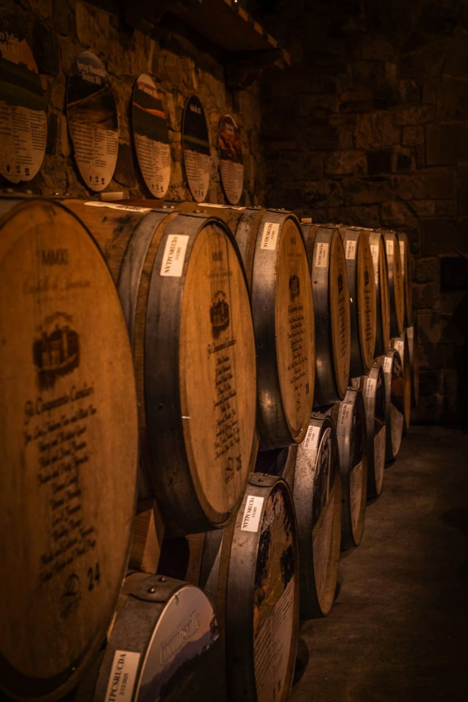 Botti di vino in legno accatastate in una cantina poco illuminata.